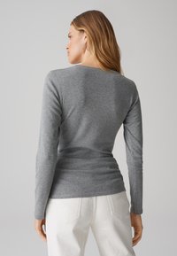 Grijze langemouwen top met een getailleerd ontwerp, zachte textuur en ronde halslijn, gecombineerd met witte jeans en minimale stikseldetails.