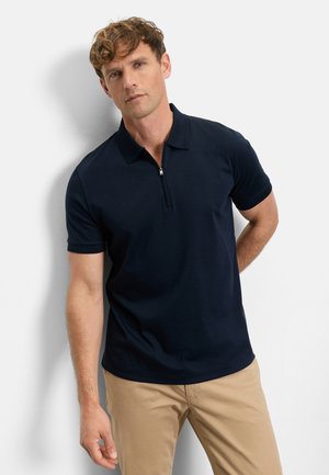 Navy polo shirt with short sleeves and a zippered collar, made from smooth fabric, paired with light khaki pants.