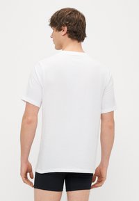 Balta medvilninė marškinėlių suapvalintu kaklu, trumpomis rankovėmis ir laisvu siluetu. Nėra matomų logotipų ar raštų. Lygi tekstūra.