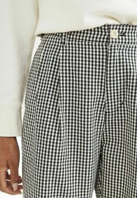 Pantaloni a scacchi bianco e nero con pieghe, chiusura con un bottone e un tessuto strutturato.