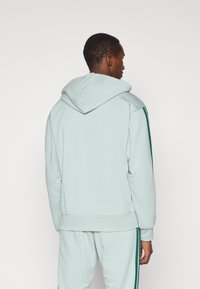 Gaiši zils kapucis ar plašu kapuci, ribotām aprocēm un apakšmalu; rotāts ar zaļām svītrām plecu un sānu daļās.