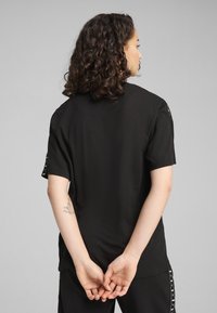 Camiseta negra de manga corta con un corte relajado, que presenta una textura suave y detalles de logo en las mangas.