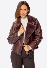 Bordowy kurtka z ekoskóry z szerokim, puszystym kołnierzem i kieszeniami na zamek. Posiada krótki fason i miękką podszycie z polarowego materiału.