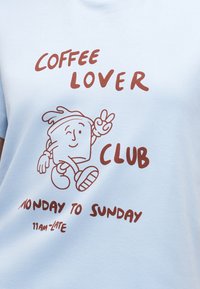 Κείμενο "Coffee Lover Club" και "Δευτέρα έως Κυριακή 11 π.μ. - αργά" με καρτούν περπατώντας φλιτζάνι καφέ που δείχνει το σήμα ειρήνης σε ανοιχτό ύφασμα.