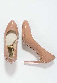 Escarpins en cuir verni nu avec un bout pointu, un haut talon aiguille, et une petite découpe sur le côté, ornés d'accents dorés.