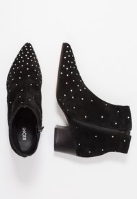 Schwarze Wildleder-Stiefeletten mit spitzen Zehen, verziert mit weißen Strasssteinen. Sie verfügen über einen seitlichen Reißverschluss und einen klobigen Holz-Absatz.