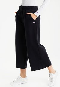 Sorte, brede sweatpants med snor i taljen, sidelommer og broderet logo. Stoffet er blødt og struktureret.