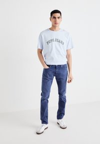 Svetlo modra bombažna majica s prosto napisanimi "PEPE JEANS" v temnem tisku, kombinirana z temno modrimi kavbojkami in belimi supergami. Enostaven, sproščen videz.