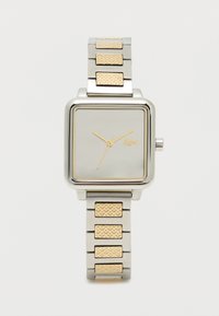 Ruudu kujuline hõbe käekell kuldsete aktsentidega, metallist rihm, millel on tekstuuriga kuldlingid, minimalistlik valge nägu kuldsete käte ja logoga.