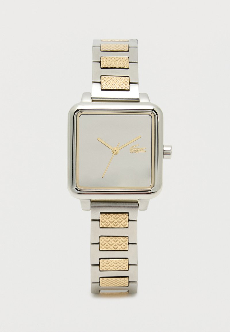 Ruudu kujuline hõbe käekell kuldsete aktsentidega, metallist rihm, millel on tekstuuriga kuldlingid, minimalistlik valge nägu kuldsete käte ja logoga.