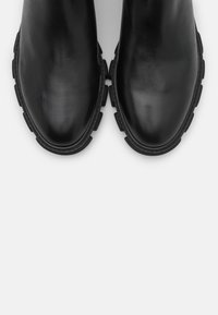 Mustat nahkaiset nilkkasaappaat, joissa on sileä pinta, pyöreä kärki ja paksu, teksturoitu kumipohja, jossa on voimakkaat urat.