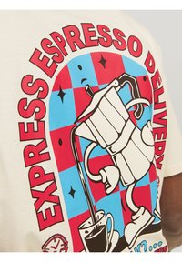 Hvid bomulds T-shirt med et grafisk motiv af en moka-kande, der hælder kaffe, sat mod en rød og blå ternet baggrund med fed tekst.