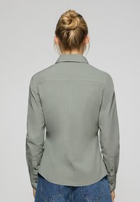 Ljusgrön knapp-up skjorta med långa ärmar, krage och en strukturerad baksida. Tillverkad av glatt tyg, har knappade manschetter och en skräddarsydd passform.