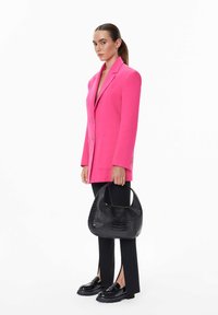 Horkou růžová oversized blazer s dvěma předními kapsami, spárovaná s černými rozšířenými kalhotami, strukturovanou černou kabelkou a masivními černými botami.