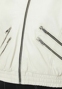 Witte leren jas met meerdere schuine ritsen, geribde tailleband en een gladde textuur. Ritsen zijn metallic met een contrasterende afwerking.