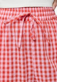 Shorts a quadri gingham rossi e rosa con vita elastica e stringa abbinata. Realizzati in un tessuto leggero e testurizzato.