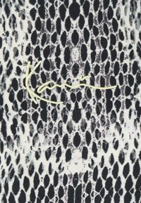 Czarna i biała tkanina w wzór węża o gładkiej fakturze, z pochyłym, żółtym haftowanym logo z napisem "Kari" na dolnej krawędzi.