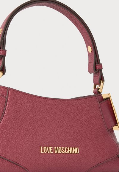Детайл в близък план на чанта Love Moschino от бордо кожа с релефна зърнеста текстура, извита дръжка и обков и лого в златист цвят.