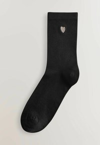 Calcetín de algodón negro con un puño acanalado y un pequeño corazón plateado bordado cerca de la parte superior. Textura suave, forma de calcetín estándar.