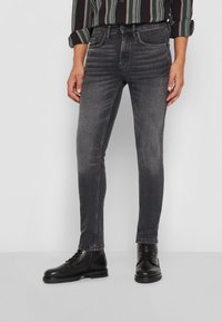 Temno sivi skinny jeans z rahlim zbledeljem, s petimi žepi, kontrastnim šivom in gladkim denim materialom. Oblečeni z črnimi škornji.