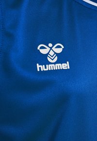 Blå sporttyg med en vit Hummel-logotyp med en unik bi-design. Slät yta och lätt material.