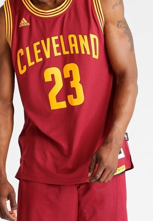 Man met een maroonkleurige Cleveland basketball-shirt nummer 23 en bijpassende korte broek, met zichtbare tatoeages op de armen.