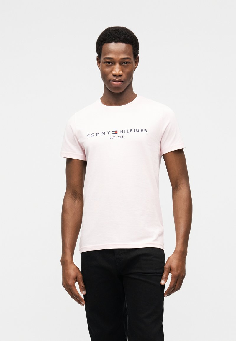 Ροζ βαμβακερό T-shirt με κοντά μανίκια, με το λογότυπο "TOMMY HILFIGER" σε ναυτικό μπλε τυπωμένο στο στήθος. Μαύρα τζιν.