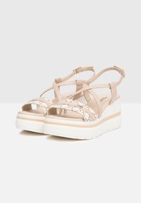 Sandali platform beige con cinghie incrociate e un accento testurizzato. Presentano una suola bianca con una sottile linea beige. Cinturino alla caviglia regolabile.