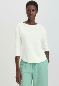 Leichtes, cremefarbenes Hemd mit 3/4-Ärmeln, rundem Halsausschnitt und einer weichen Textur, kombiniert mit lockeren, mintgrünen Hosen.