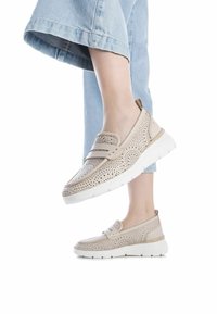 Zapatos slip-on perforados en color beige con una superficie texturizada, suela blanca y dos cintas en el empeine; combinados con denim azul claro.