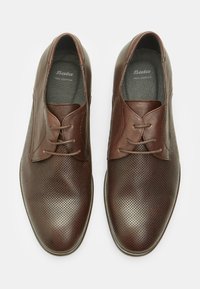 Scarpe in pelle marrone con design perforato, chiusura con lacci, finitura liscia e punta arrotondata, etichettate "Bata Pelle Vera."