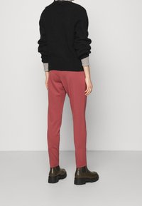 Zwarte, chunky gebreide trui met poffende mouwen, gecombineerd met slim-fit, stoffige rozenkleurige broek en donkerbruine enkellaarzen.