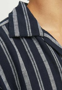 Koszula z krótkim rękawem w granatowym kolorze z naprzemiennymi białymi paskami. Posiada kołnierzyk w szpic oraz teksturowaną fakturę.