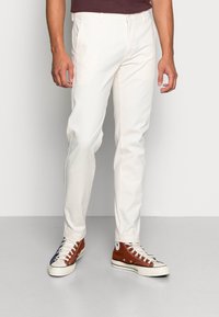 Pantaloni slim-fit bianchi realizzati in tessuto misto cotone, con chiusura a zip e tasche frontali, abbinati a sneaker alte marroni e blu navy.