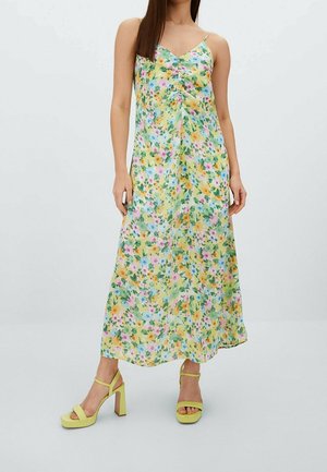 Floral Maxikleid in hellem Gelb mit pinken, orangenen und grünen Mustern. Das Kleid hat dünne Träger und eine drapierte Silhouette. Daneben gelbe High-Heelsandalen mit quadrater Spitze und Blockabsatz.