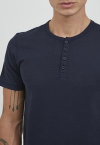 Marineblå bomull T-skjorte med rund hals, kort erm og en frontlomme med fem knapper. Jevn tekstur og tettsittende design.