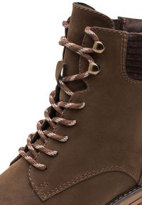 Bottine en cuir brun avec une finition texturée, dotée de lacets ronds marron et crème, d'œillets en métal et d'un col rembourré pour plus de confort.