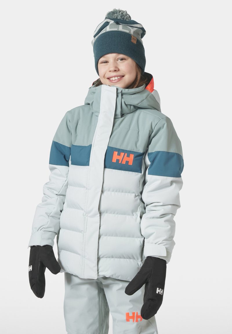 Nafouknutá světle šedá a tyrkysová izolační bunda s oranžovým logem, kapucí a černými rukavicemi, kterou má na sobě dítě; zasněžené pozadí.