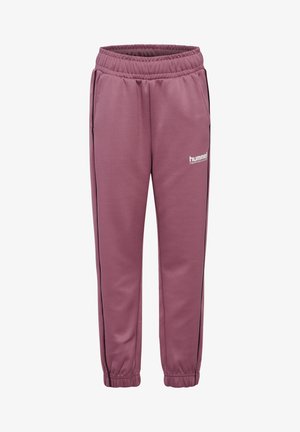 Dreng iført lilla træningsdragt med sorte striber og sorte sneakers, stående mod en ensfarvet grå baggrund.