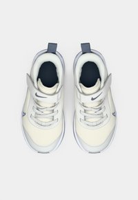 Baskets Nike blanches avec une tige en mesh, des accents gris, une sangle ajustable et une semelle en caoutchouc. La vue de dessus montre un design lacé et le logo.