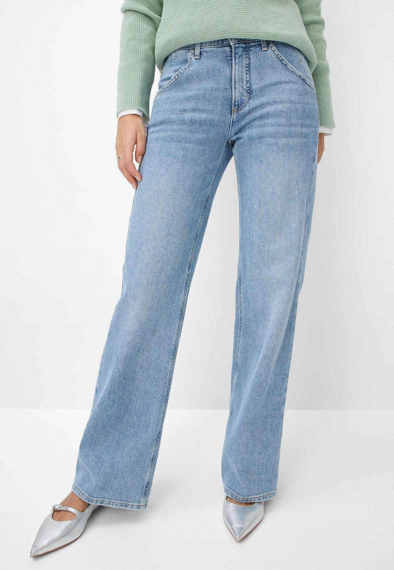 Lichtblauwe, wijde jeans gemaakt van denim; heeft voorzakken, riemlussen en een licht vervaagde textuur, gecombineerd met zilveren puntige schoenen.
