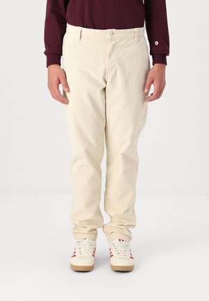 Beige corduroy pants with a slim fit, featuring front pockets and a button closure, paired with white sneakers with red stripes.