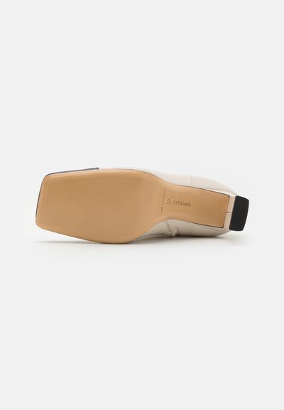 Beige leren schoen met een vierkante neus en een lage blokhak. Gladde textuur met een zwarte accent bij de hak en een rubberen zool.