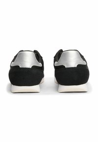 Schwarze Sportschuhe mit silbernen Akzenten, ausgestattet mit einer glatten Lederferse und einem strukturierten Stoff-Obermaterial, das eine abgerundete Zehenform und eine weiße Sohle zeigt.