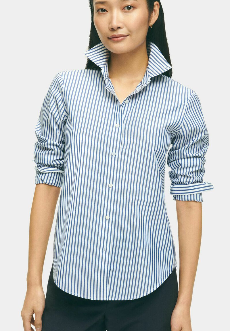 Camicia a righe blu e bianche con colletto alto, maniche arrotolate e tessuto liscio. Orlo curvo.