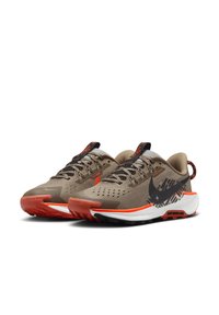 Zapatillas atléticas en color beige con acentos negros y naranjas. Presentan una parte superior de malla transpirable, superposiciones texturizadas y una suela distintiva con un patrón de agarre.