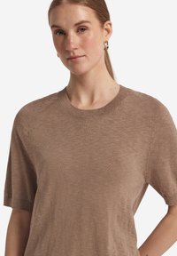 Brun kortærmet sweater i let strik med ribbede kanter og raglanærmer. Glat tekstur, afslappet pasform, minimal detaljering.