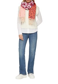Gilet en tricot crème porté sur une chemise blanche, associé à un jean bleu et des sneakers blanches. Une écharpe à imprimé animal multicolore avec des franges complète le look.