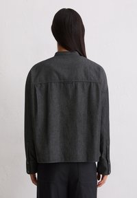 Camicia in denim grigio con vestibilità relaxed, maniche lunghe, polsini con bottone e dettagli sulla spalla posteriore. Texture liscia e design minimale.