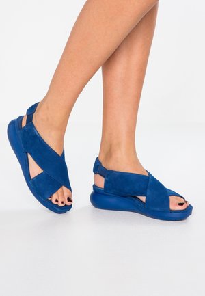 Blue suede sandals with a crisscross design, open toe, and cushioned sole. Features a back strap for support and textured sole for grip.